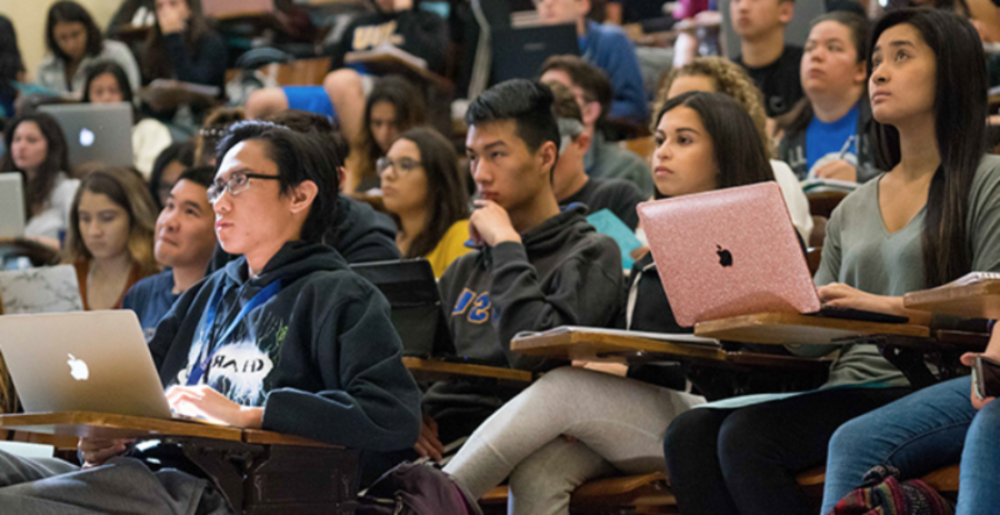 Students in classroom taking notes on laptops and notebooks